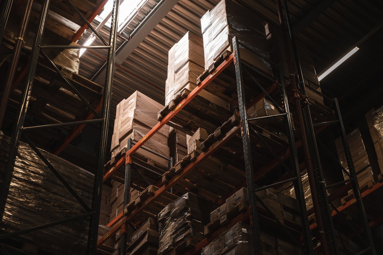 hero-img-02 Interior view of a warehouse with stacked cardboard boxes on high shelves, showcasing storage and logistics.